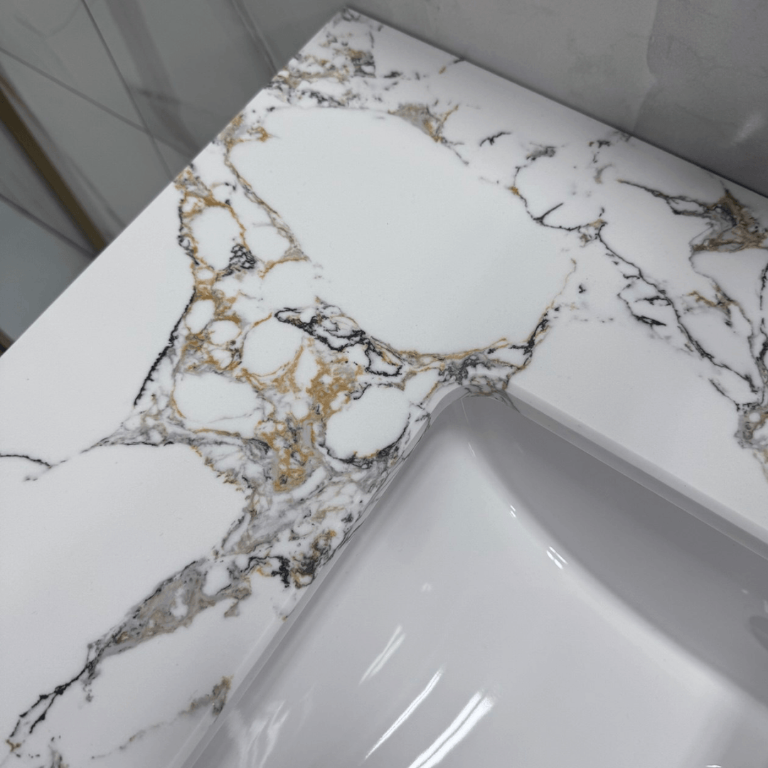 Gros plan sur la surface d'un comptoir en marbre blanc avec des veines dorées complexes et une partie de l'évier encastré, typique des vanités de salle de bain de luxe.