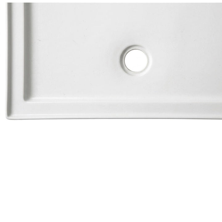 Gros plan sur la finition blanc lustré et le drain d'une base de douche en acrylique pour alcôve, illustrant la qualité du matériau et les brides de carrelage
