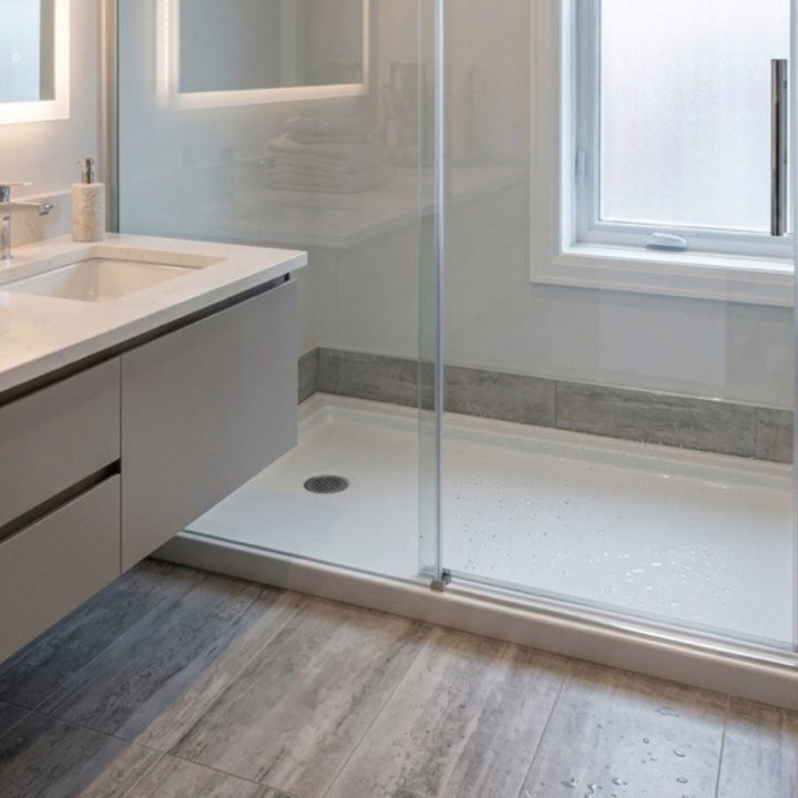 Aménagement moderne d'une salle de bain avec une base de douche en acrylique blanche installée en alcôve, accompagnée de portes en verre et d'une vanité grise