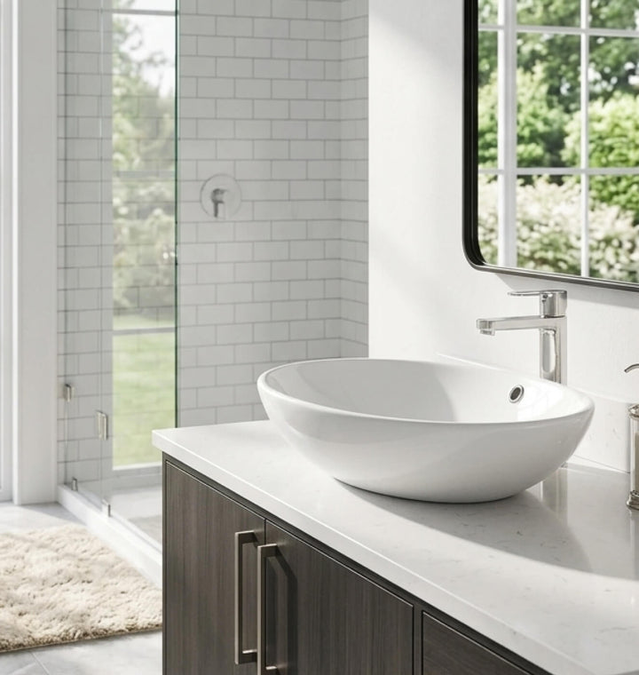 Une salle de bain moderne et lumineuse avec une élégante vasque ovale en céramique blanche posée sur un meuble en bois foncé. Ce lavabo salle de bain de style contemporain est doté d'un lavabo profond pour plus de fonctionnalité. En arrière-plan, on aperçoit une douche vitrée et une fenêtre donnant sur un jardin verdoyant.