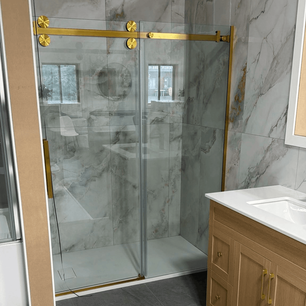 Porte de douche coulissante en verre avec quincaillerie dorée et galets de roulement apparents, installée dans une salle de bain avec carrelage mural effet marbre et meuble-lavabo en bois